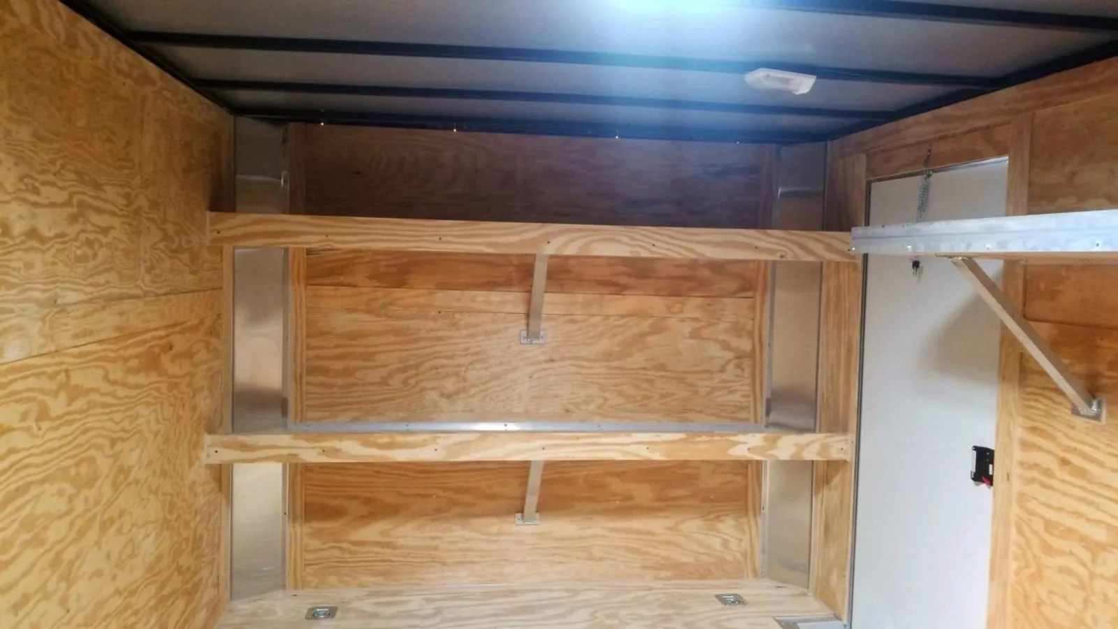 Enclosed trailer interior upfitted with wall shelving, E-track, and floor tie-down rings